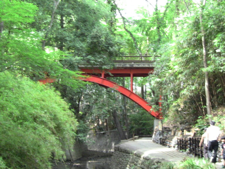 The red Golf Bridge arching over the green ravine at Todoroki Valley