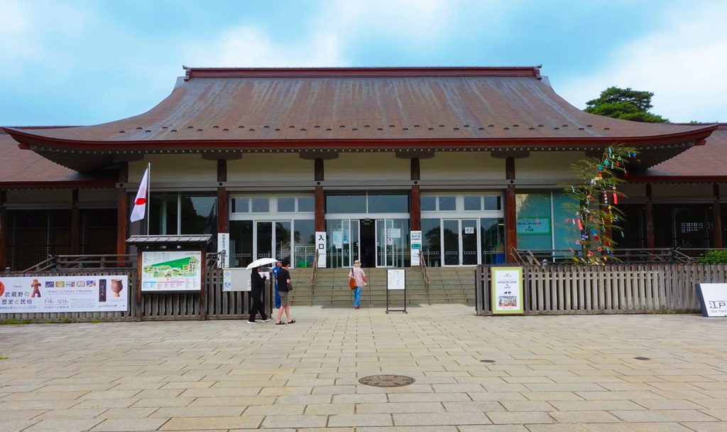 Entrance to the Edo Tokyo Open Air Architectural Museum, a wide tiled roof over glass doors with tanabata bamboo beside them