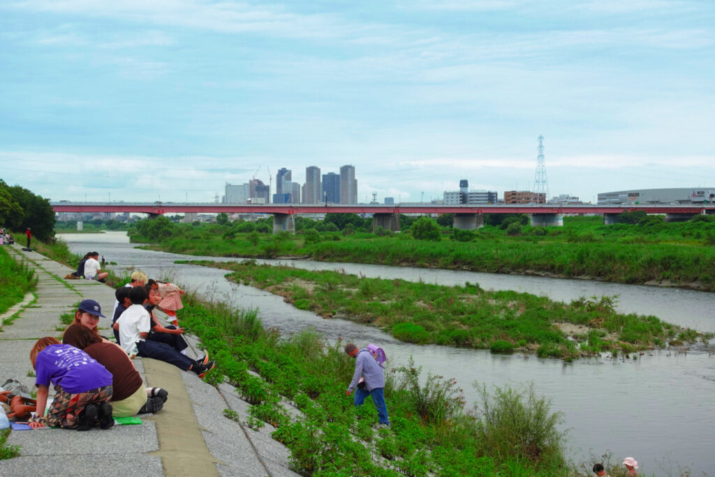 People picnicking on the Tama River bank at Futako Tamagawa with the Tokyo skyline behind