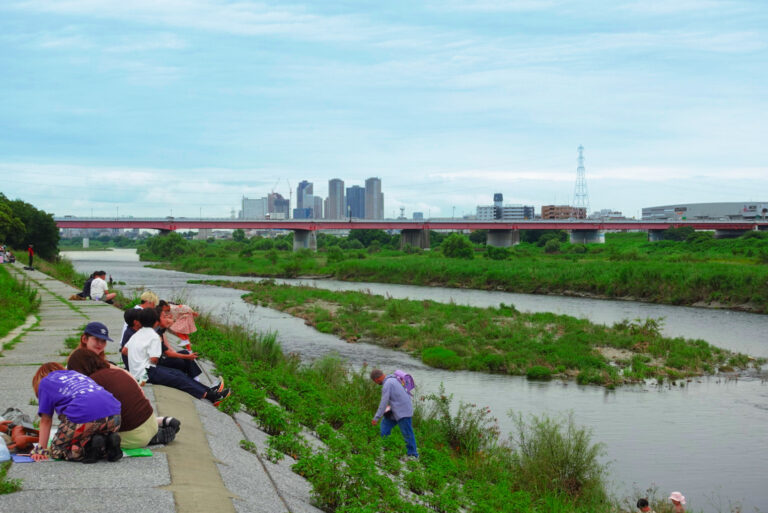 People picnicking on the Tama River bank at Futako Tamagawa with the Tokyo skyline behind