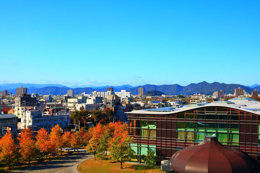 Gifu Media Cosmos seen across the plaza with autumn trees and mountains behind