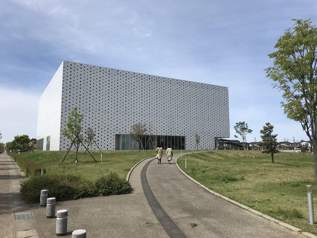 The perforated white facade of Kanazawa Umimirai Library from the approach path
