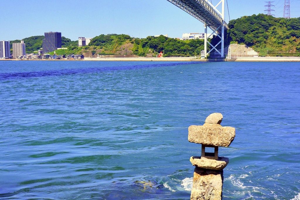 A stone lantern standing in the Kanmon Strait in front of Mekari Shrine, with the Kanmon Bridge and Shimonoseki across the water A stone lantern standing in the Kanmon Strait in front of Mekari Shrine, with the Kanmon Bridge and Shimonoseki across the water