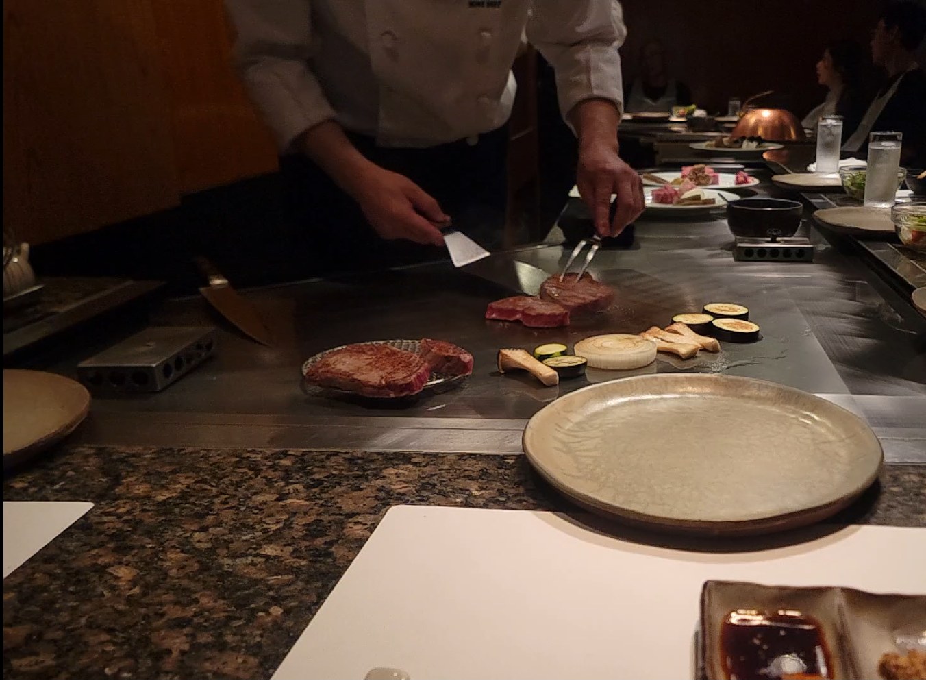 Teppanyaki chef grilling Kobe beef steaks and vegetables on an iron griddle at a Kobe restaurant