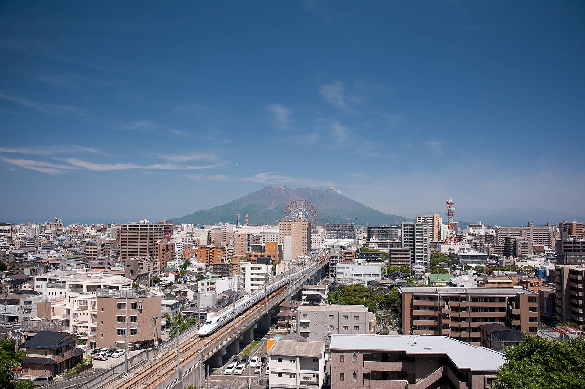 Kyushu Shinkansen N700 train arriving at Kagoshima-Chuo above the city, with Sakurajima volcano behind