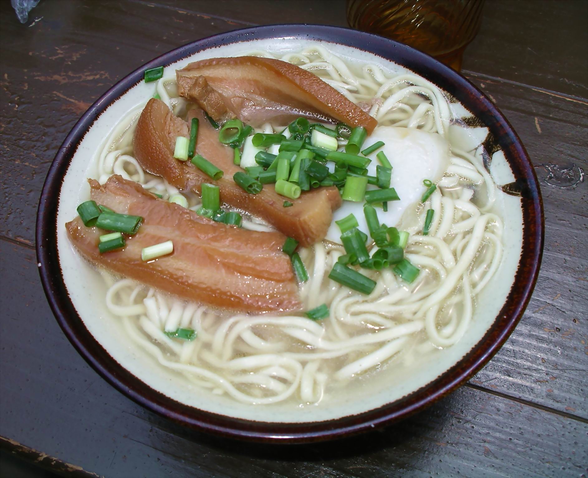 A bowl of Okinawa soba with braised pork belly, green onion and thick wheat noodles