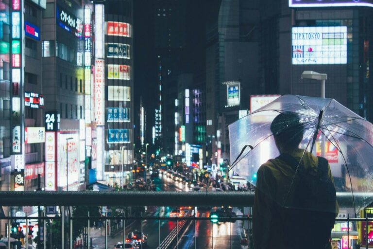 Rainy day Tokyo: a person with a clear umbrella in front of Shinjuku buildings at night
