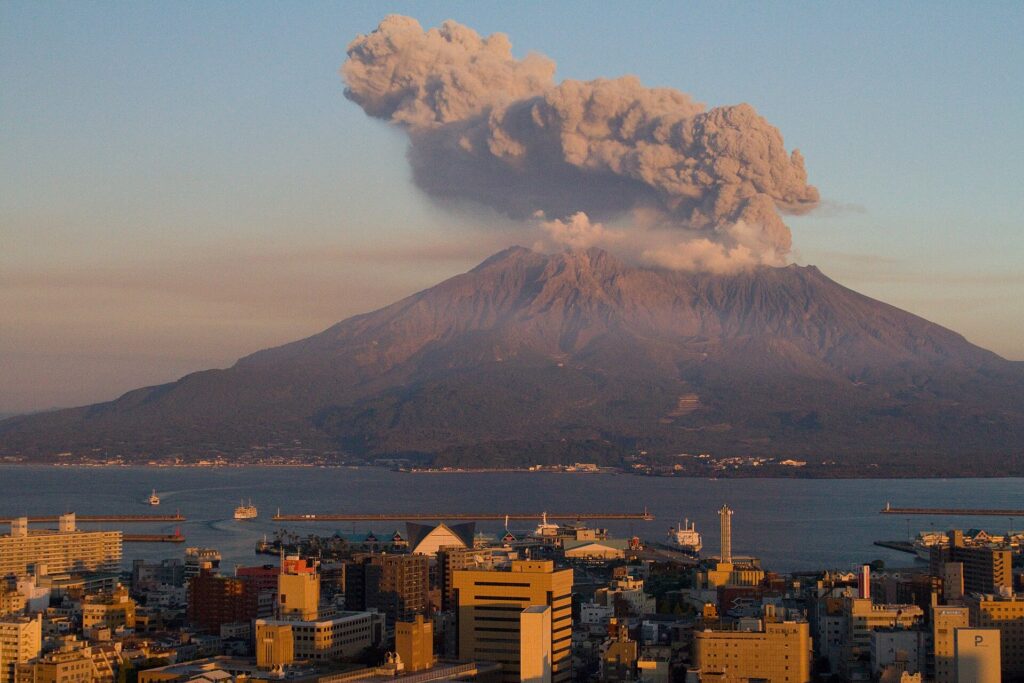 Sakurajima volcano erupting an ash plume at sunset across Kagoshima Bay, seen from Kagoshima city